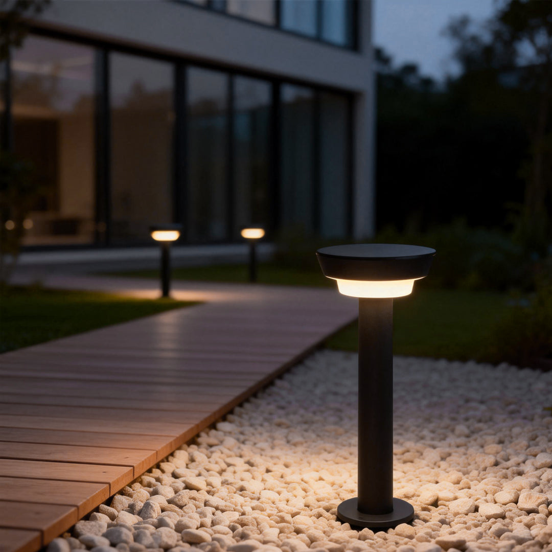 Solar powered garden path lights highlighting a wooden deck edge and pebble landscaping near a modern home exterior.