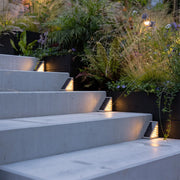 Solar powered lights for steps illuminating a modern outdoor staircase with plants and concrete stairs.