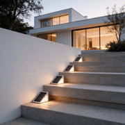 Solar powered lights for steps illuminating modern concrete stairs leading up to a white house.