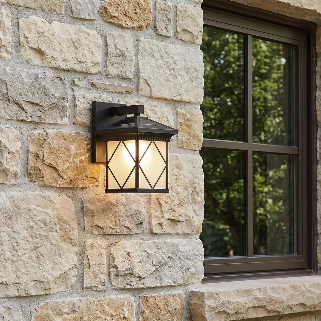 Solar powered outdoor wall sconce mounted on a stone exterior wall beside a black-framed window.