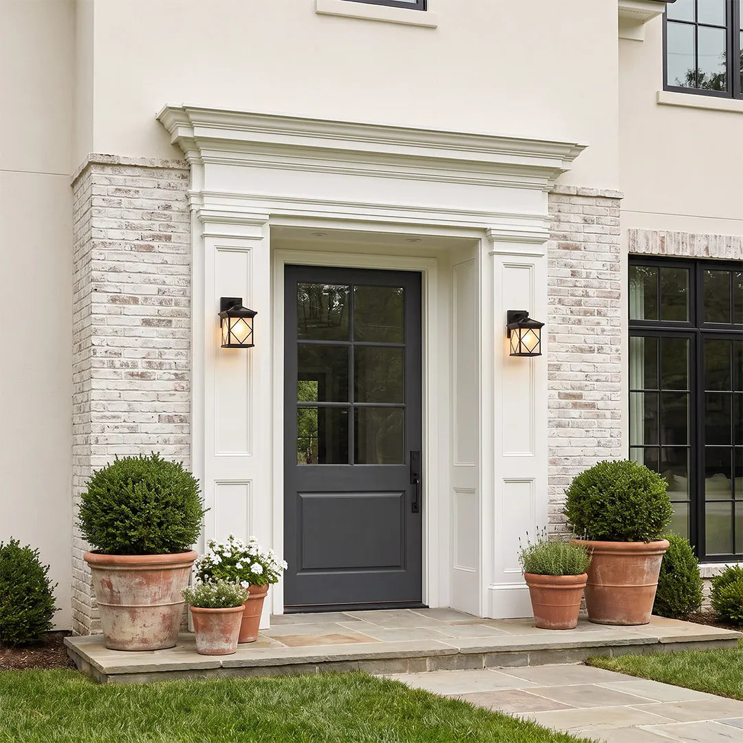 Solar powered outdoor wall sconces installed beside a front entry door on a light stone facade.