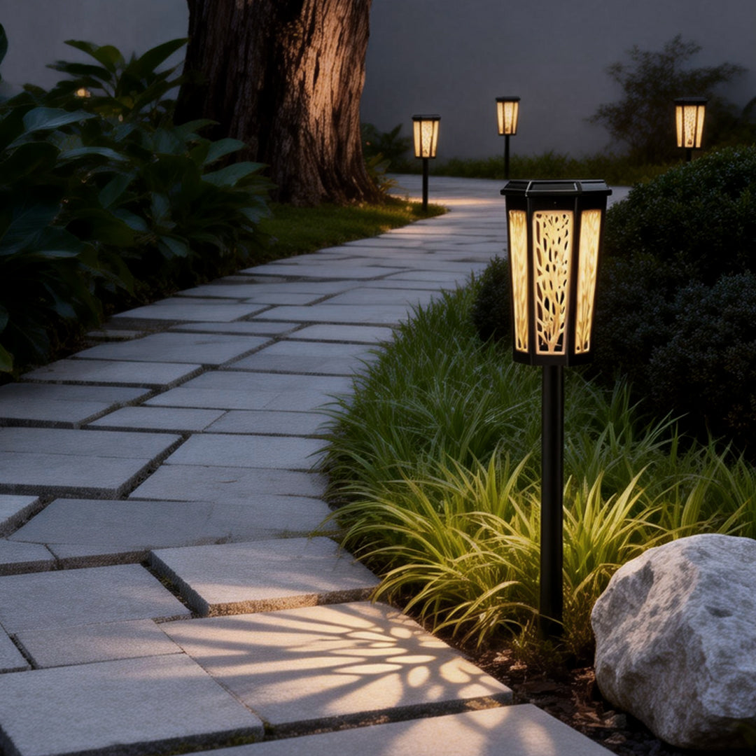 Solar stake light illuminating a stone pathway with decorative leaf patterns projected onto the ground at night.