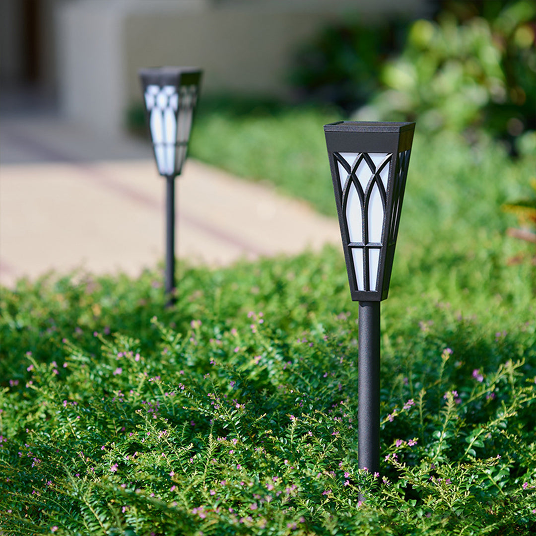 Solar stake lights with decorative metal cages installed along grass pathway border
