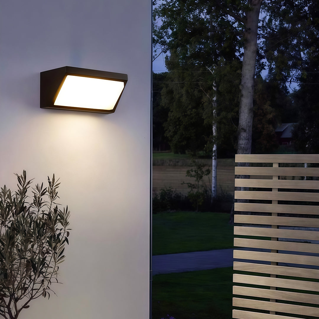 Solar-powered outdoor wall mount light installed on a brown brick wall, casting light downwards to brighten the surroundings.