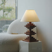 Solid wood table lamp on soft beige surface beside large window.