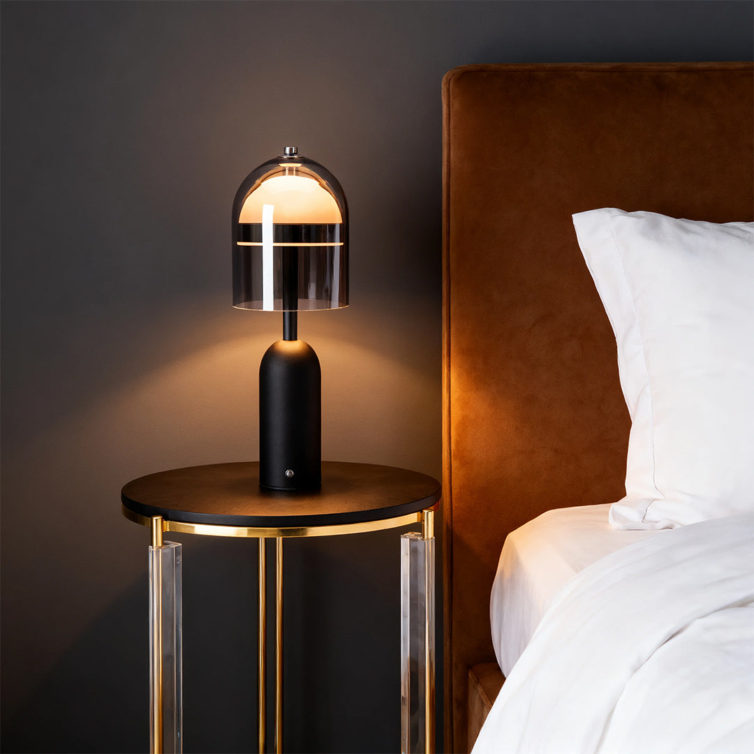 A sophisticated black glass shade table lamp providing soft illumination on a bedside table in a modern bedroom setting. 