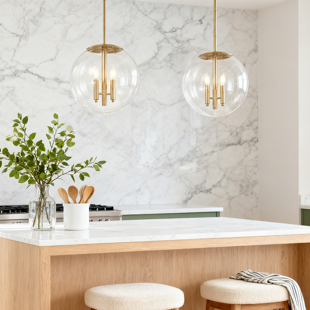 Two sophisticated clear globe pendant light fixtures illuminating a kitchen island with a striking white marble slab accent wall.
