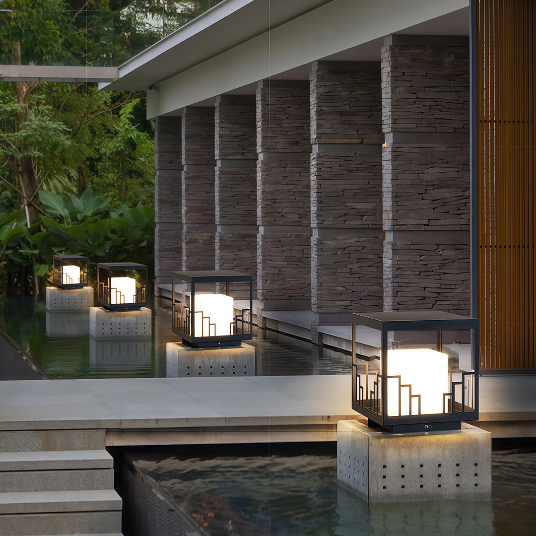 Sophisticated outdoor pillar light with glass shade chandelier design providing ambient lighting on modern home entrance pathway.
