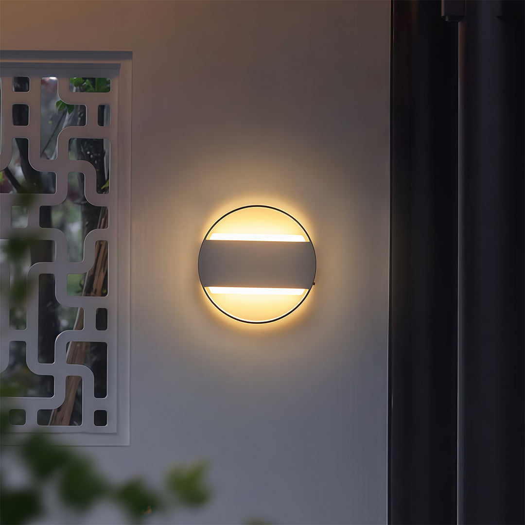 Sophisticated round wall mount exterior light with glass shade chandelier design creating warm ambient glow on dark facade.