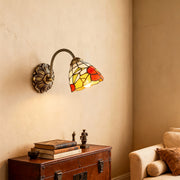 Sophisticated stained glass wall sconce lighting with glass shade chandelier influence providing accent lighting above storage chest.