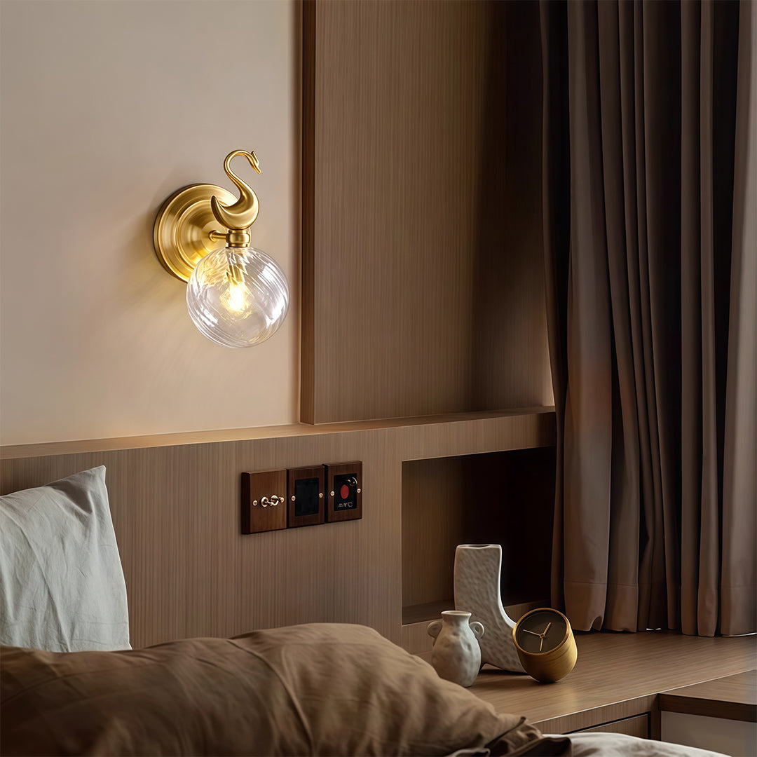 Sophisticated wall mounted LED light with glass shade chandelier influence creating warm accent glow beside modern hotel bed.
