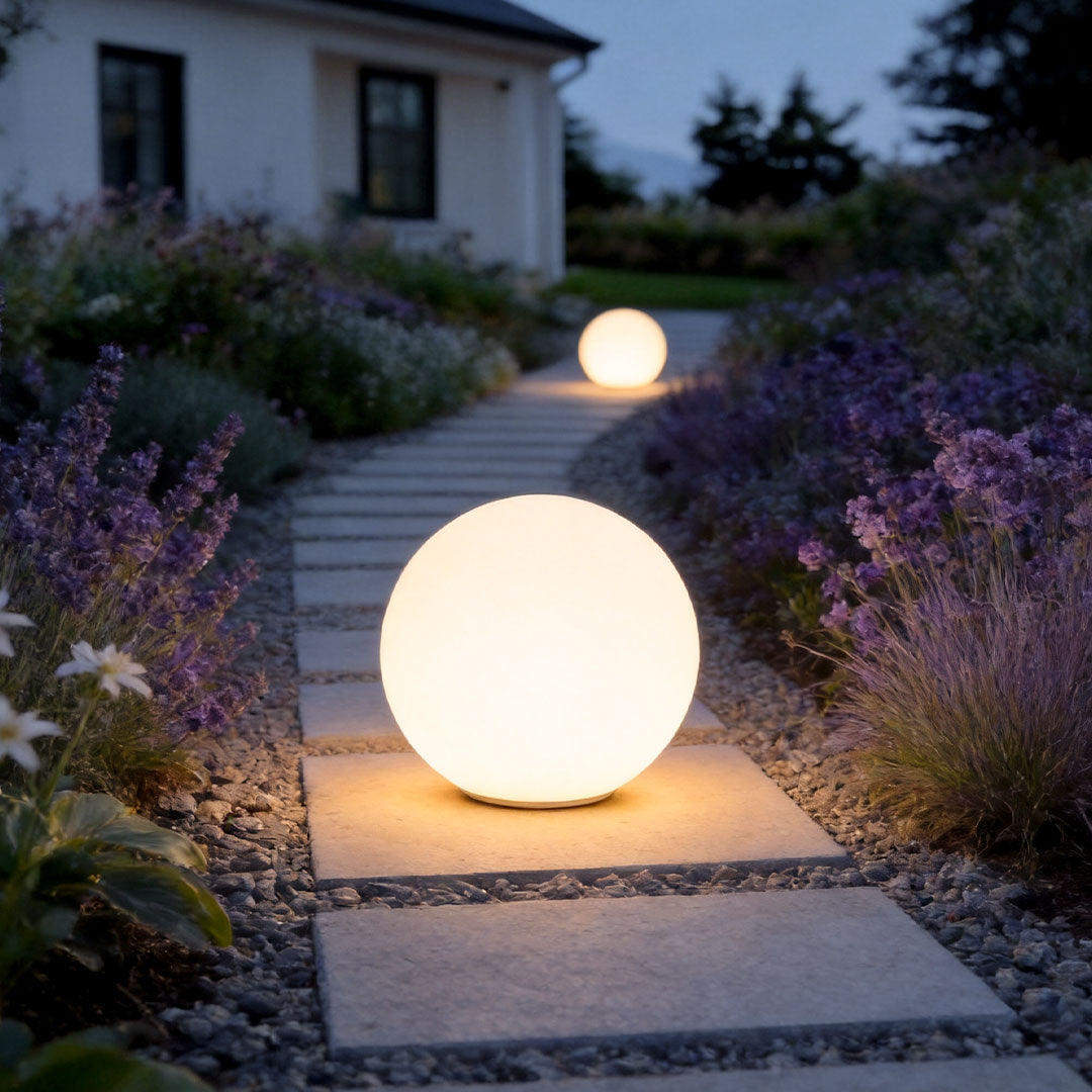 Sphere floor lamp placed along a garden pathway with soft warm outdoor illumination.