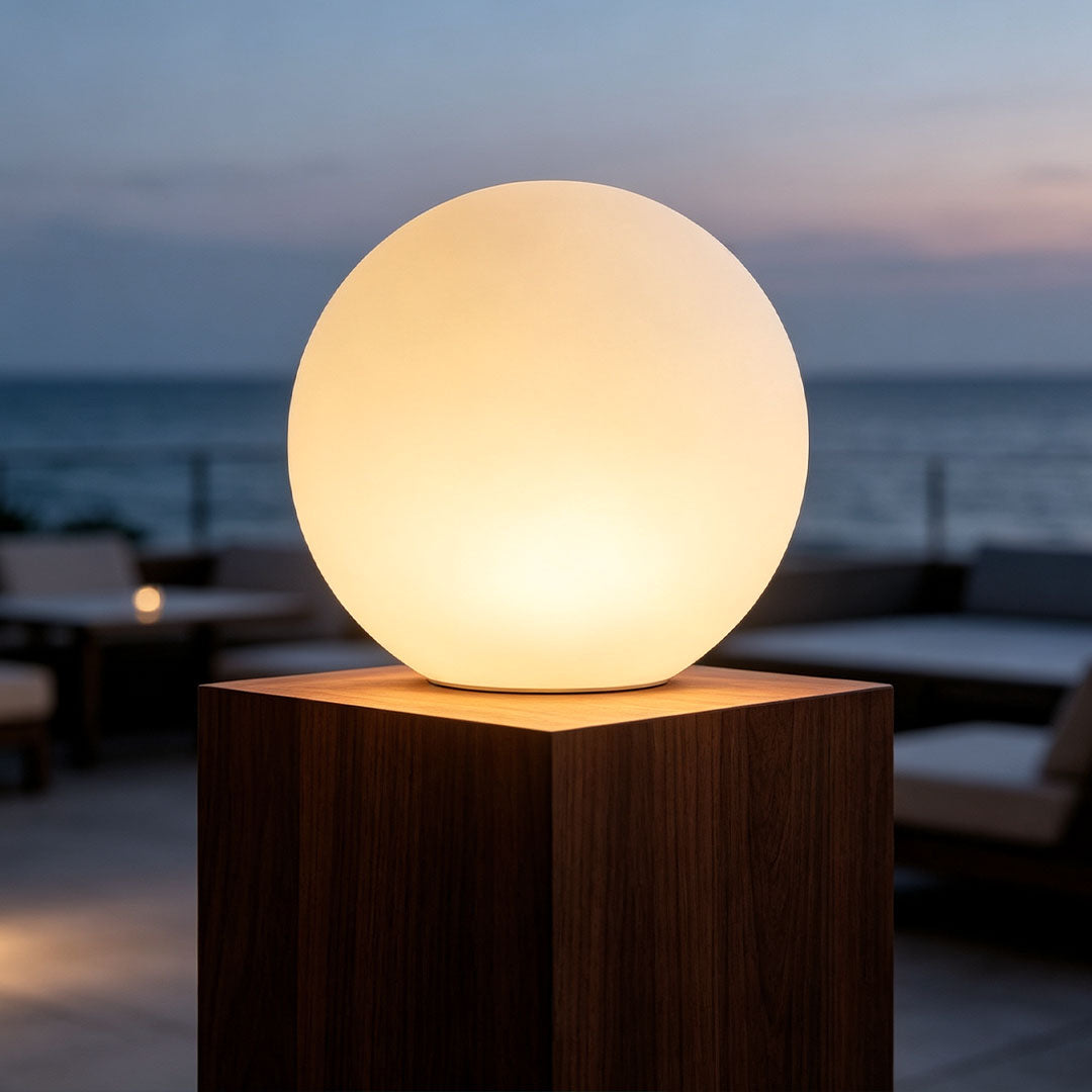 Sphere floor lamp glowing beside a modern outdoor patio lounge at sunset.
