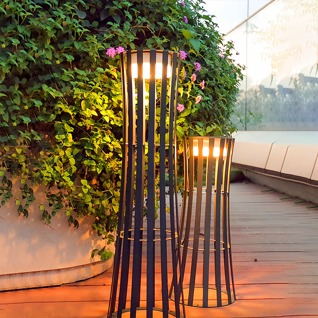 Spherical outdoor black lanterns hanging beneath a dark wooden pergola, casting ambient light on an outdoor dining table with a city view.