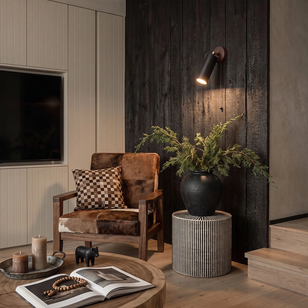Spotlight wall lights illuminating a dark wood living room corner with an accent chair and greenery.