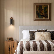 Spotlight wall lights mounted beside a bed in a warm neutral bedroom with wood furniture.
