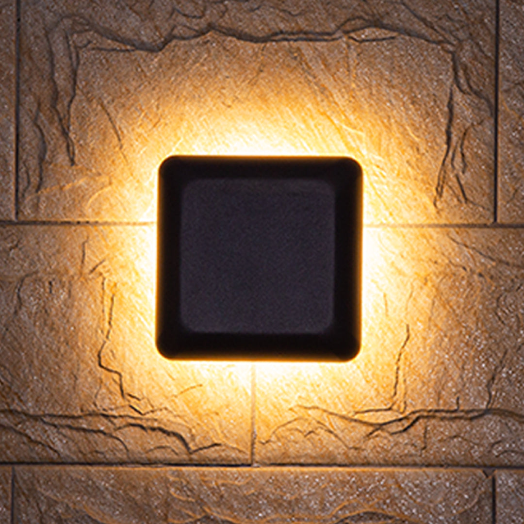 Square waterproof outdoor wall light casting warm halo illumination on beige textured stone surface