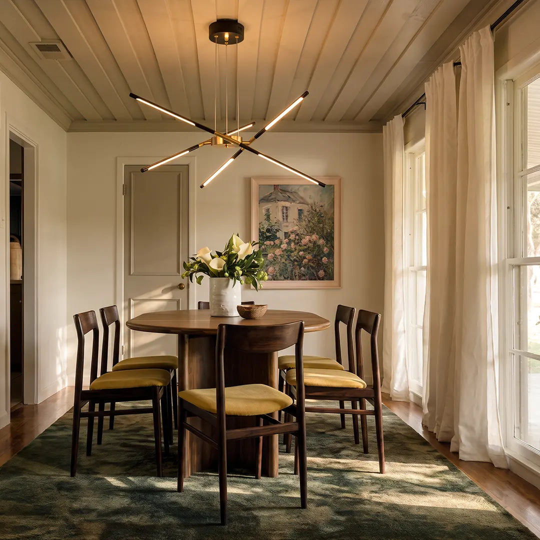 Sputnik chandelier suspended above a dining table in a bright transitional room with paneled walls, soft curtains, and classic wood chairs.