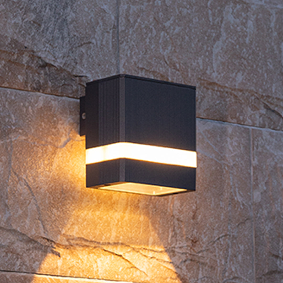 Square black garden wall light with white band casting golden light on concrete surface