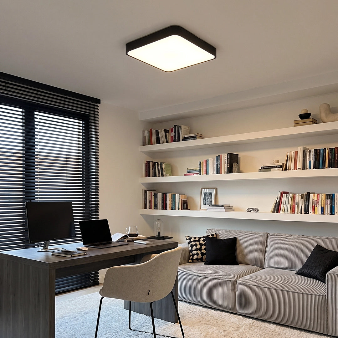 Square ceiling light with a black frame installed in a modern home office with built-in shelving and a striped sofa.