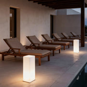 Square floor lamp illuminating a modern outdoor lounge area with sunbeds and a pool.