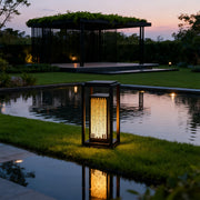 Square outdoor lantern along a pathway near a pond, offering stylish and functional lighting.