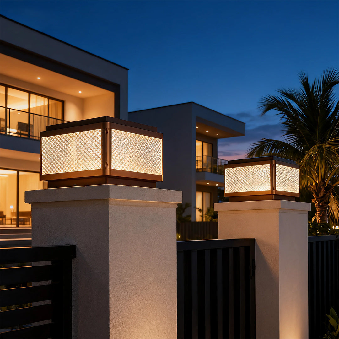 Square outdoor pillar light placed near a fence and garden, enhancing the outdoor ambiance with subtle lighting.