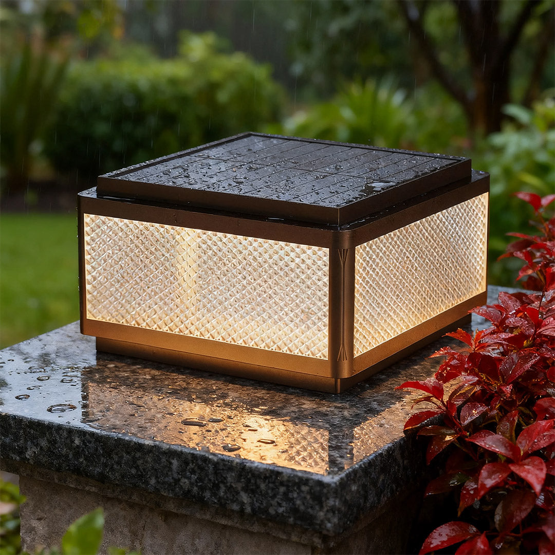 Square outdoor pillar light in a garden with a fence, adding a contemporary touch to the outdoor space.
