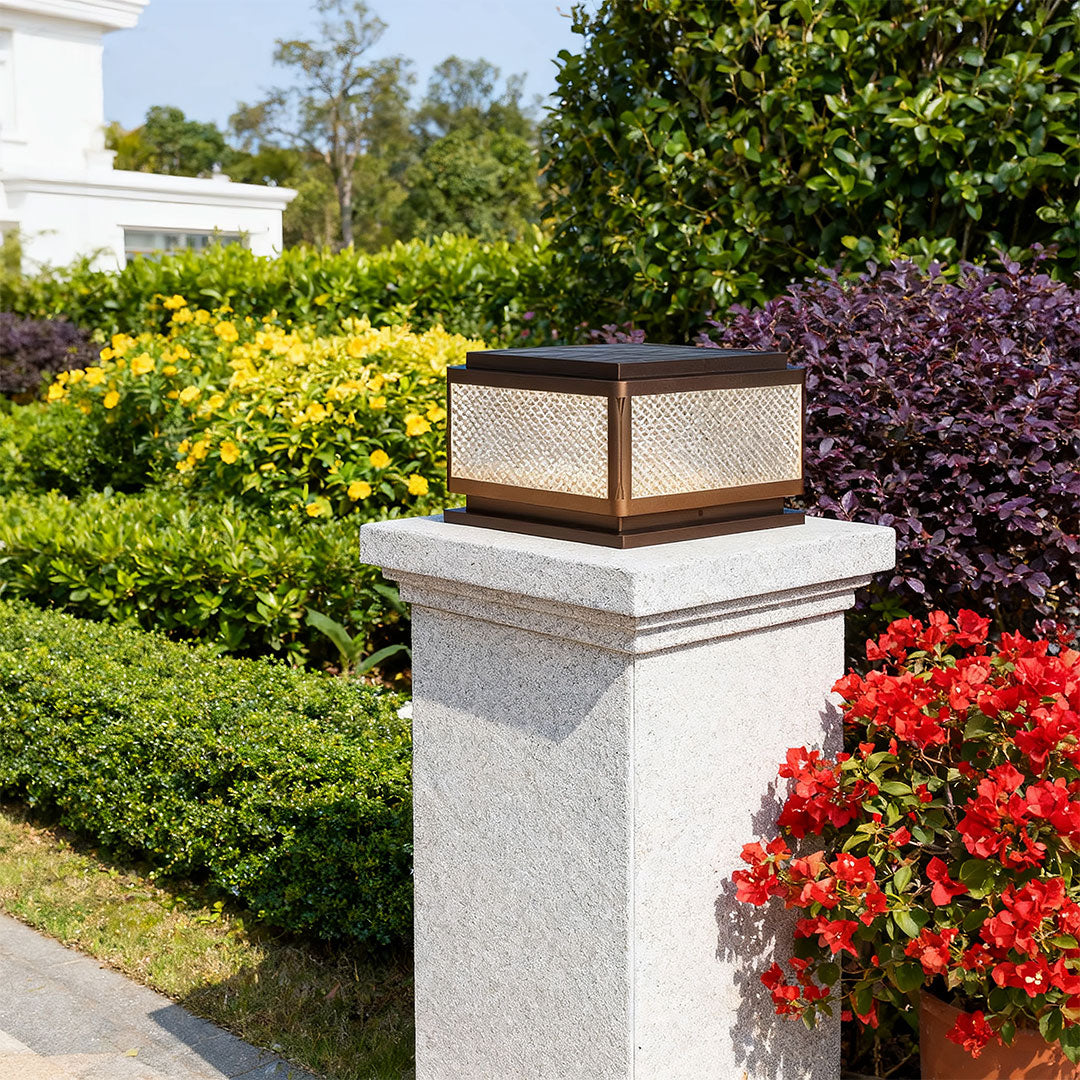 Square outdoor pillar light in a garden with a fence, adding a contemporary touch to the outdoor space.