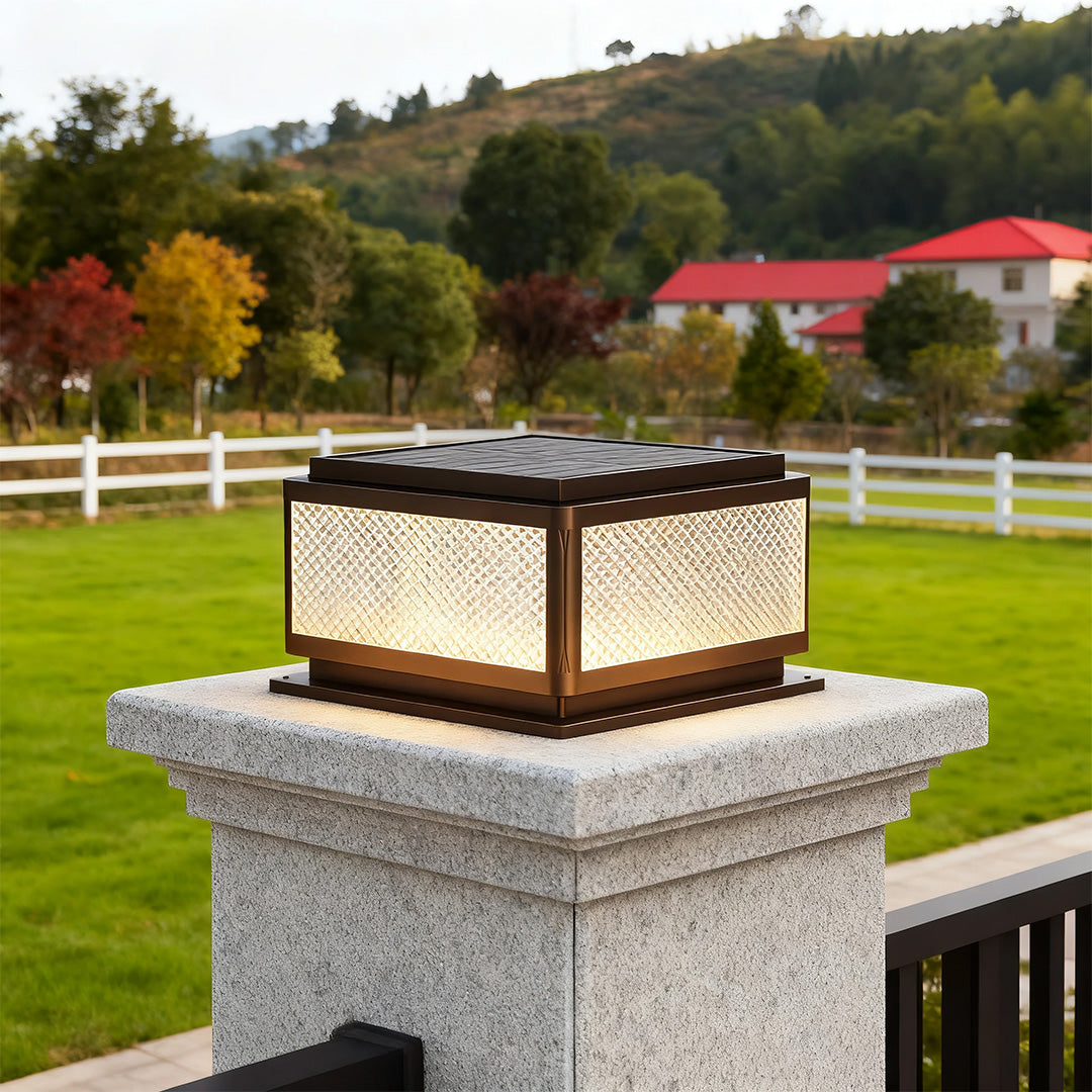 Square outdoor pillar light in a garden with a fence, adding a contemporary touch to the outdoor space.