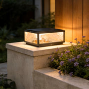 Square outdoor pillar lights installed on stone column beside a wooden exterior wall at night.