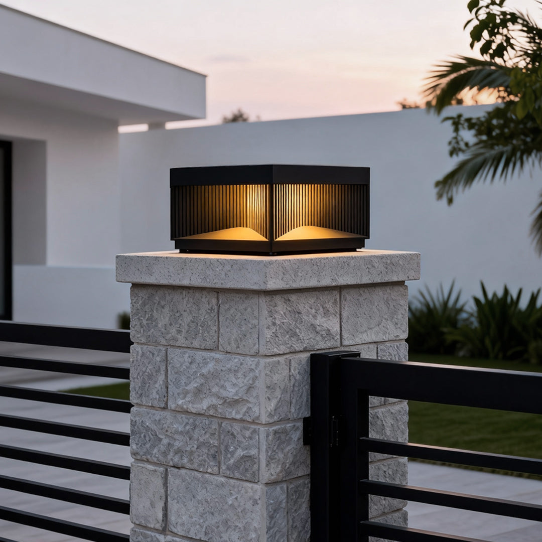 Square outdoor pillar lights installed on stone post providing warm ambient lighting in landscaped garden daytime.