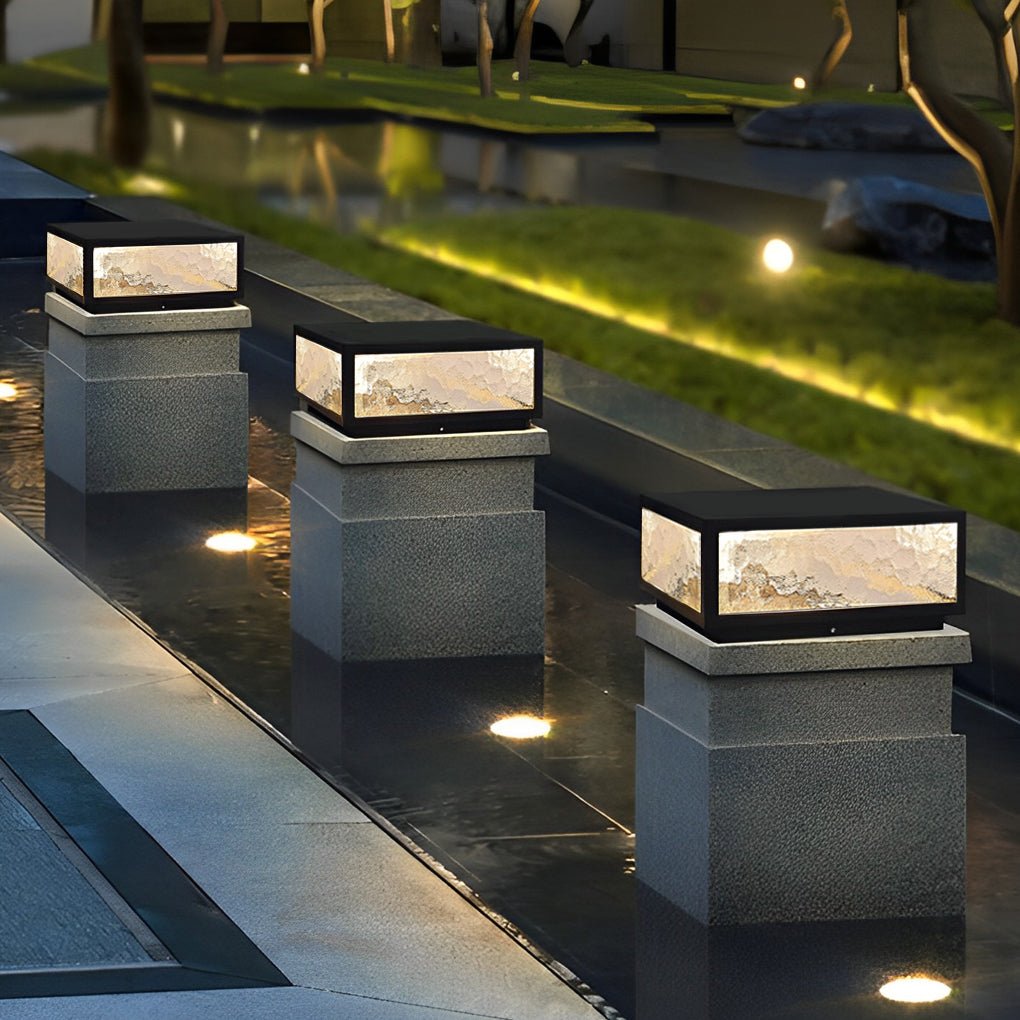 Square outdoor pillar lights aligned along a walkway beside a landscaped lawn at night.