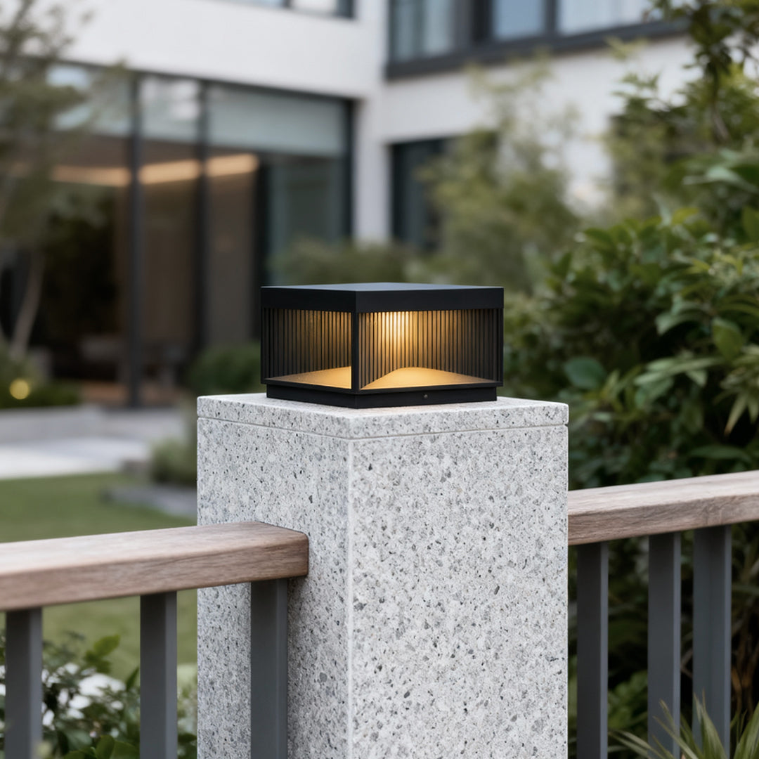Square outdoor pillar lights installed on white stone post providing warm ambient lighting in landscaped garden.