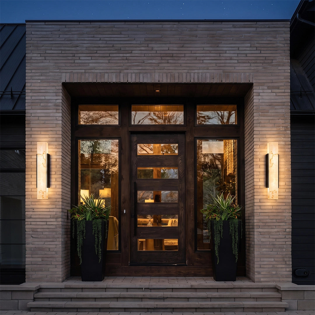 Square outdoor wall lights installed on both sides of a modern front entrance, creating warm vertical illumination on a brick exterior wall.
