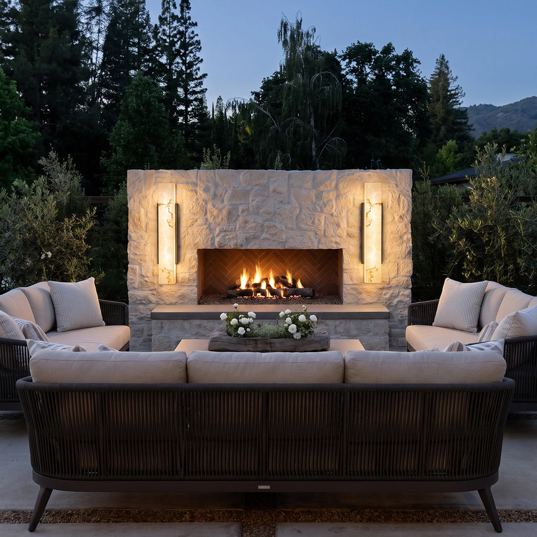 Square outdoor wall lights mounted beside a stone fireplace, adding warm architectural lighting to a cozy outdoor seating area.