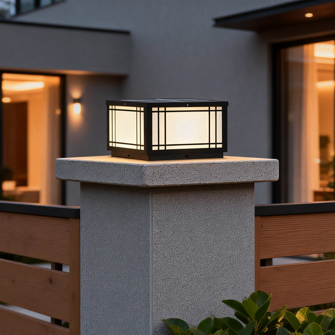 Square pillar light mounted on a concrete post outside a modern home, emitting warm ambient light for pathway and entrance illumination.