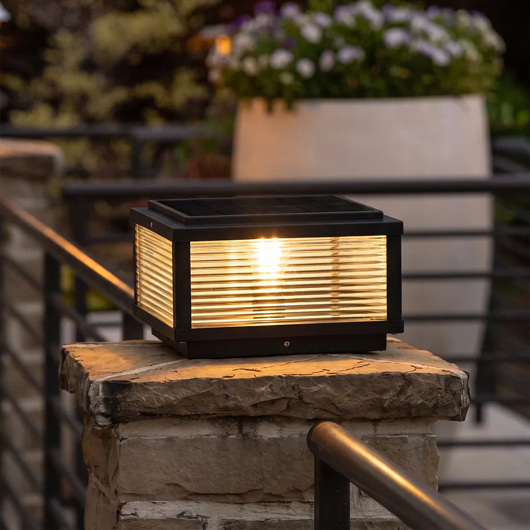 Square pillar light installed on a stone gate post, showcasing a black metal body, textured side panels, and warm ambient lighting.