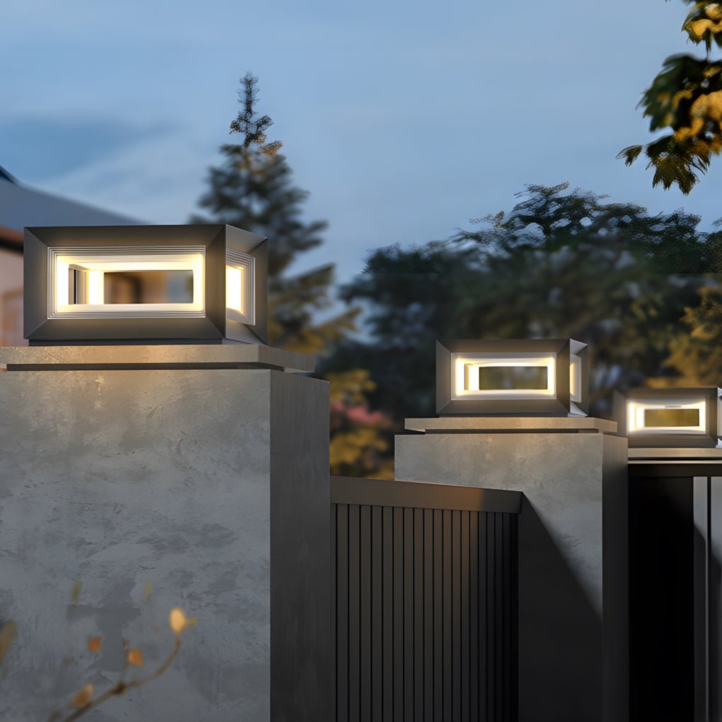 Outdoor square pillar lights mounted on tall concrete posts, illuminating a gated residential pathway at twilight.