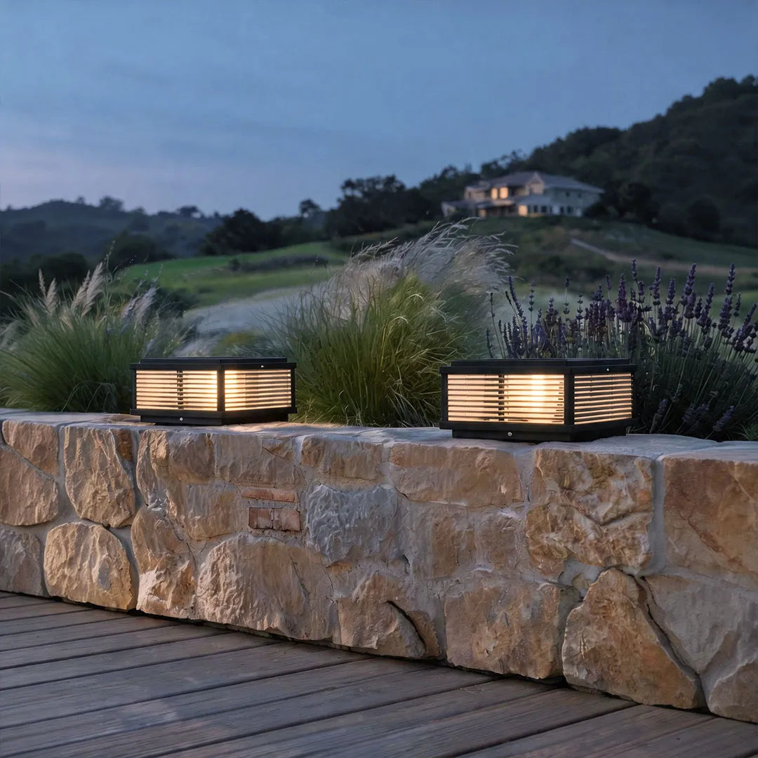 Square pillar lights installed along a stone garden wall in an outdoor landscape setting.