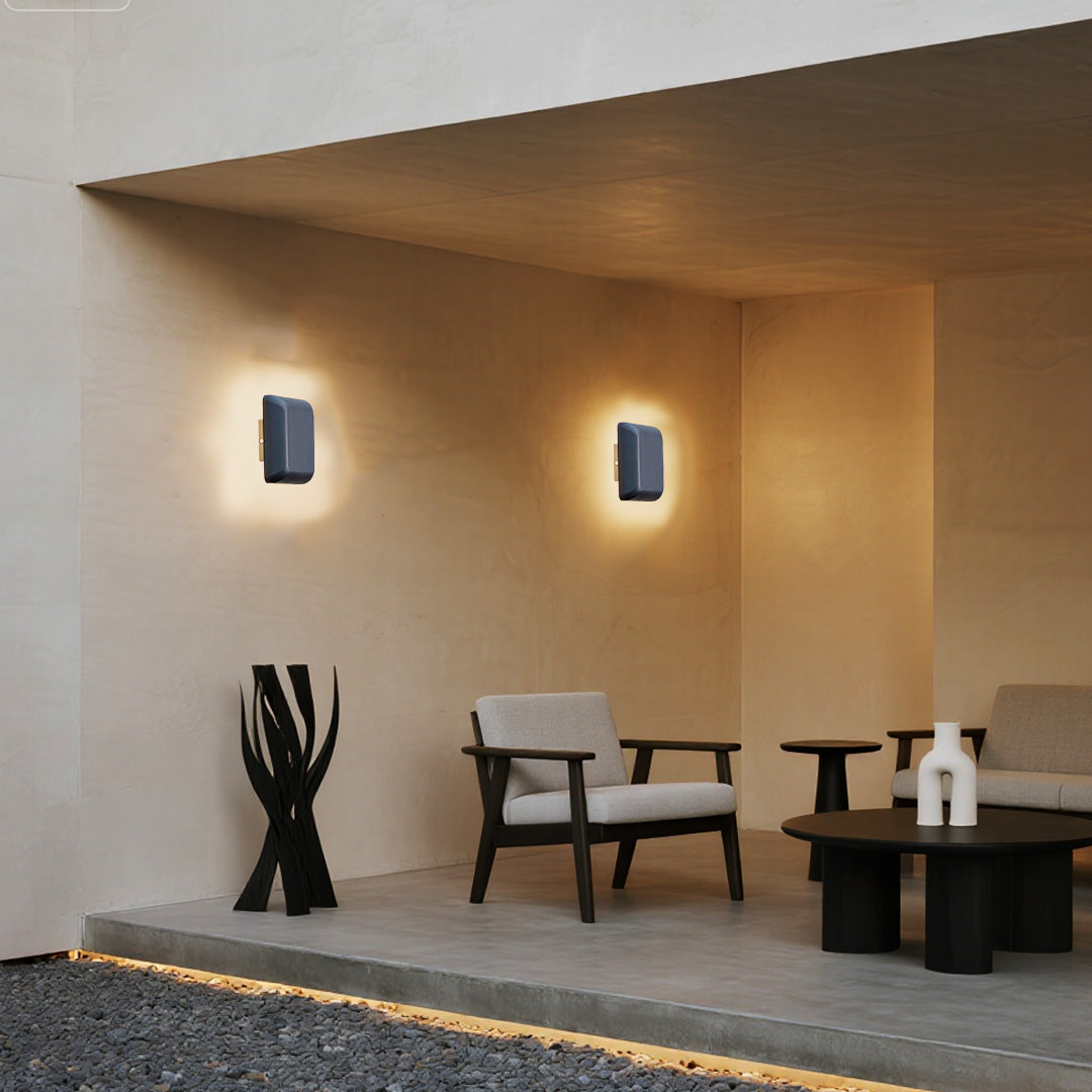 Square waterproof outdoor wall light with defined corners casting warm light on textured wall