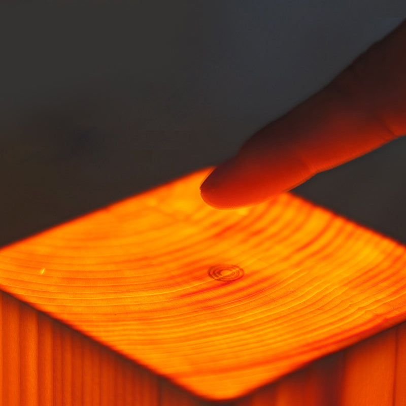Square wood lamp in small cube shape, glowing on a wooden surface.
