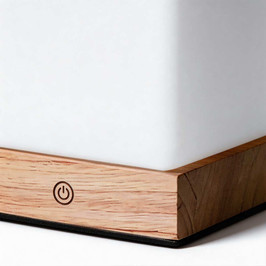 Square wood lamp with a warm light, placed on a wooden desk.