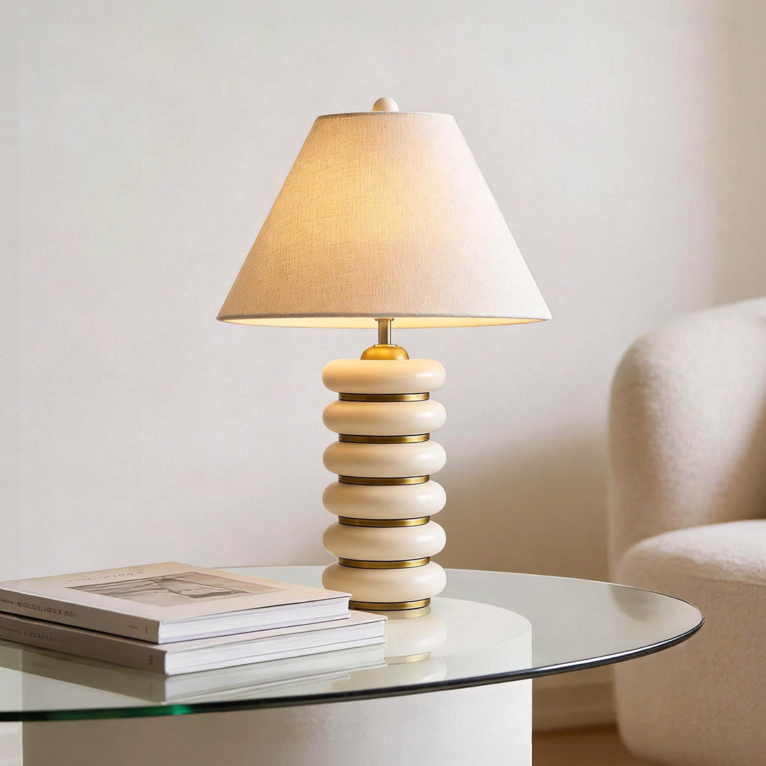 A chic cloth table lamp with a stacked cream ring base and linen shade on a glass coffee table.
