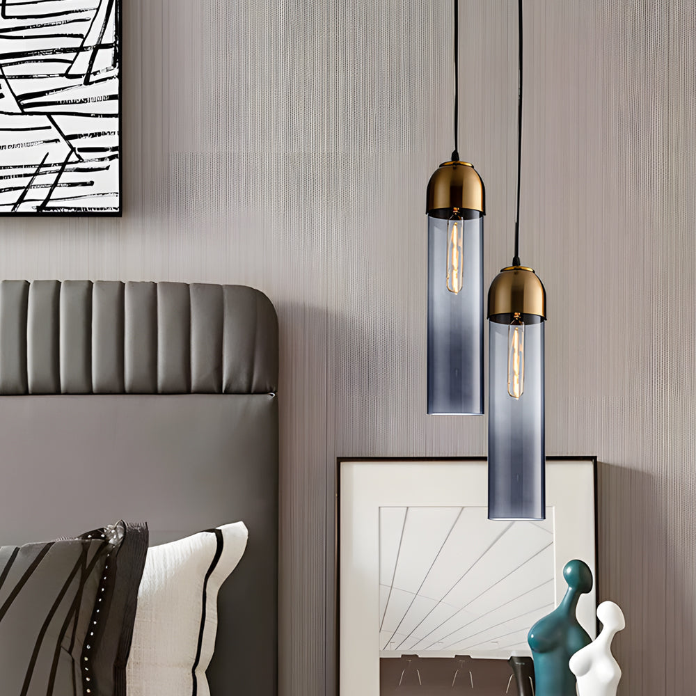 Staggered smoke grey Gold Frosted Cylinder Pendant lights over a nightstand in a modern room.