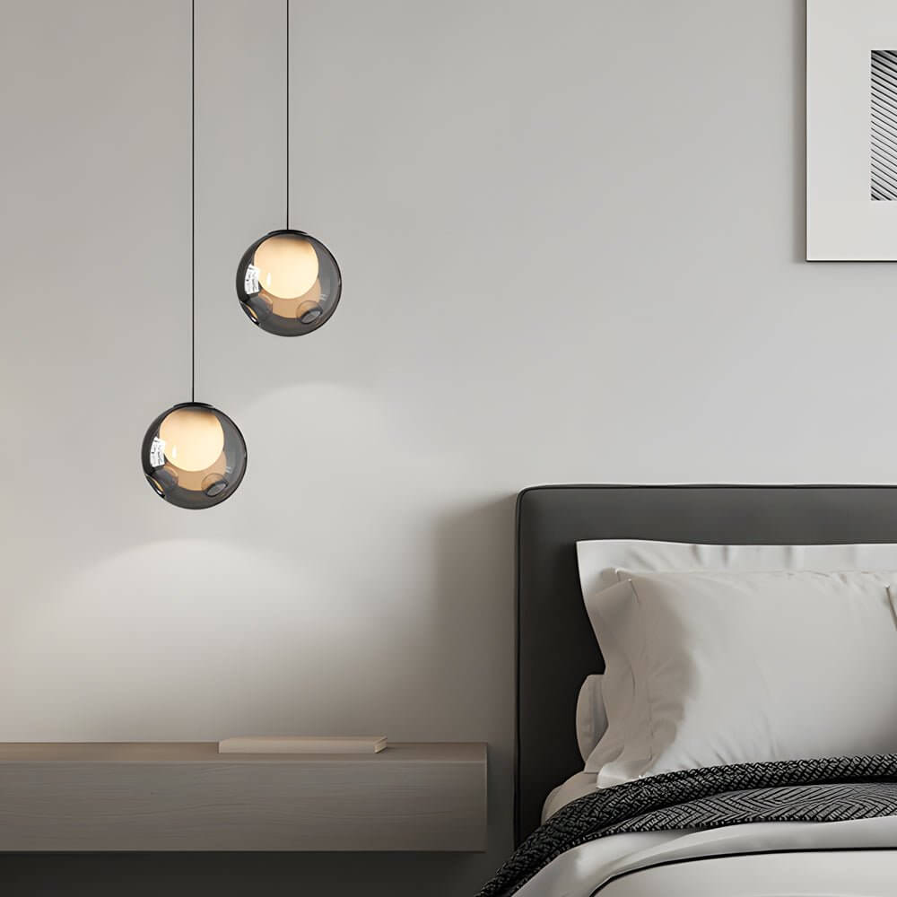 Staggered pair of smoked glass pendant lights used as elegant bedside lamps in a modern bedroom.