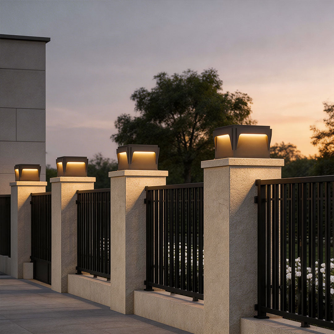 Stylish stainless steel outdoor pillar lights lining a driveway with black metal fencing at sunset.