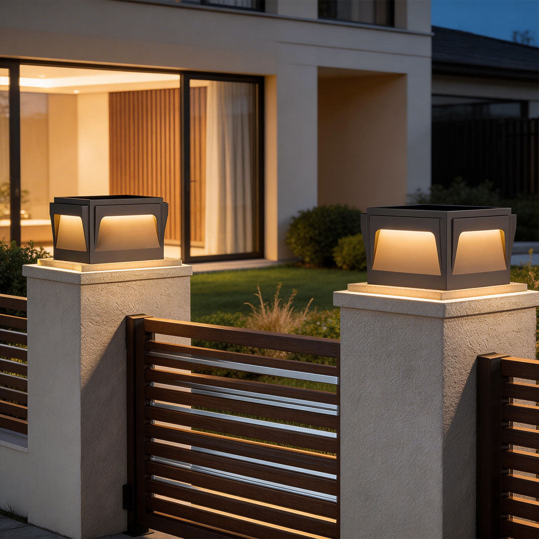 Sleek stainless steel outdoor pillar lights installed on stone pillars near a modern fence and garden.