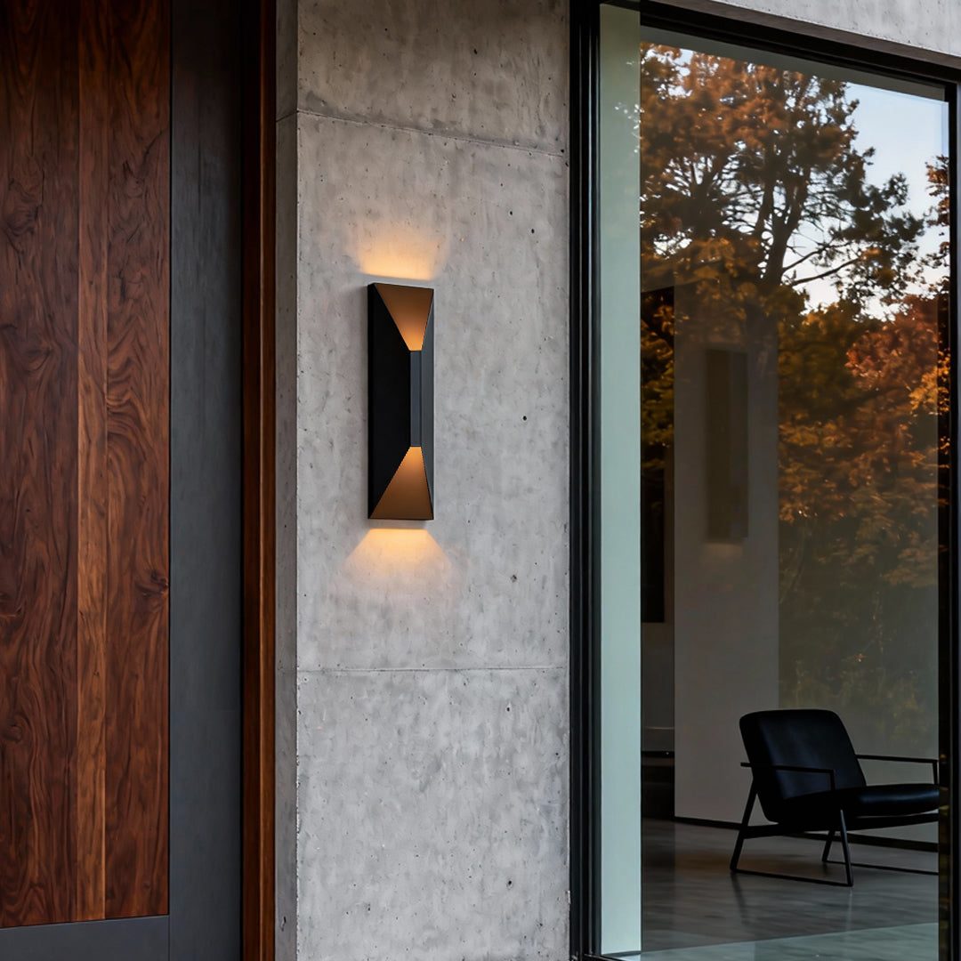 Modern stainless steel up and down wall light mounted beside a wooden and concrete exterior, illuminating the outdoor entryway.