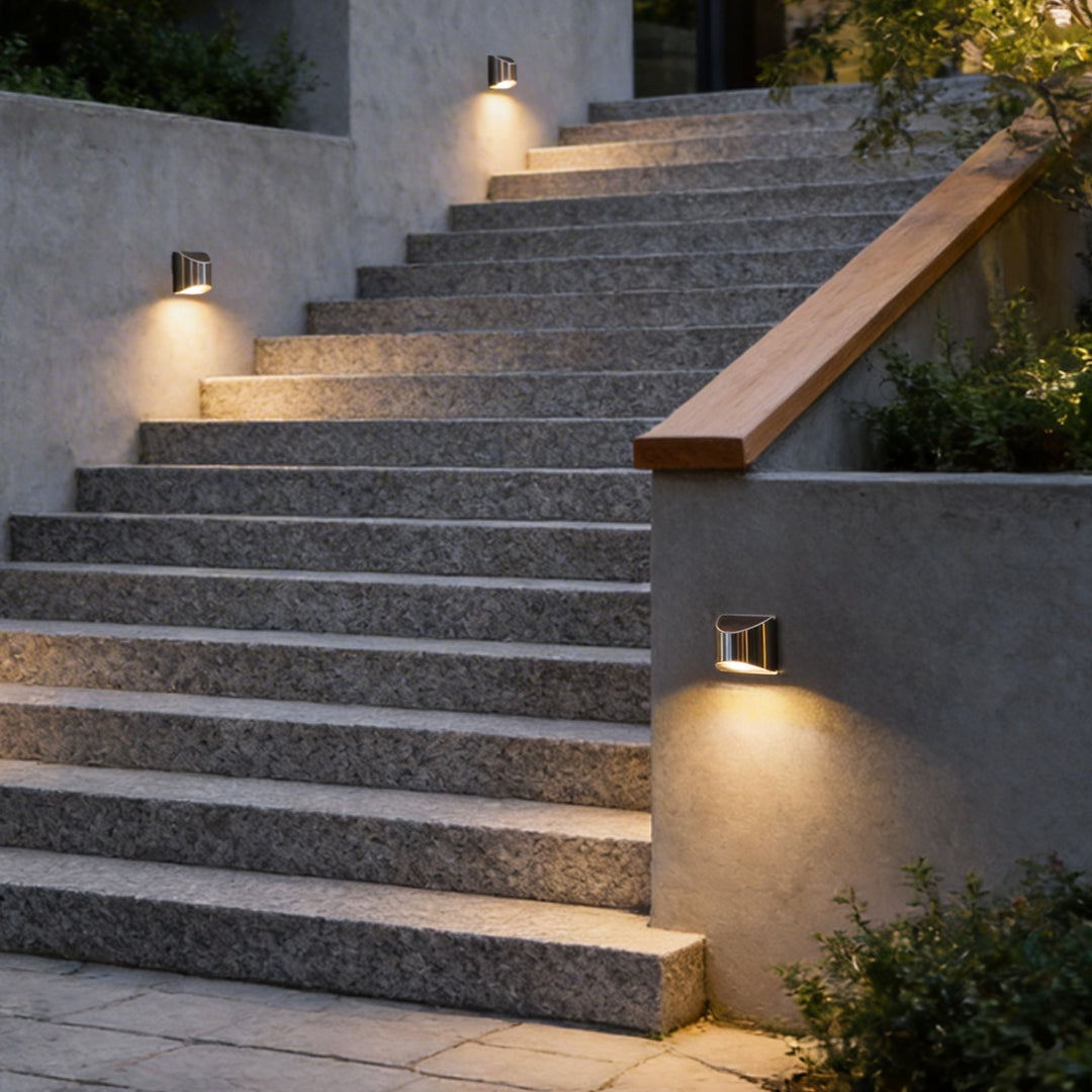 Stainless steel wall lamp illuminating outdoor steps with modern, sleek design and warm light.